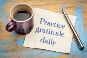 A cup of coffee over a note stating Practice gratitude daily with a pen left open